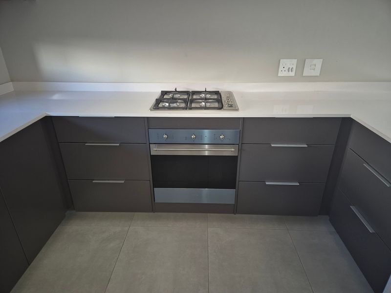Modern kitchen featuring dark grey cabinetry, white quartz countertops, a built-in gas hob, and an integrated oven with large format floor tiles.