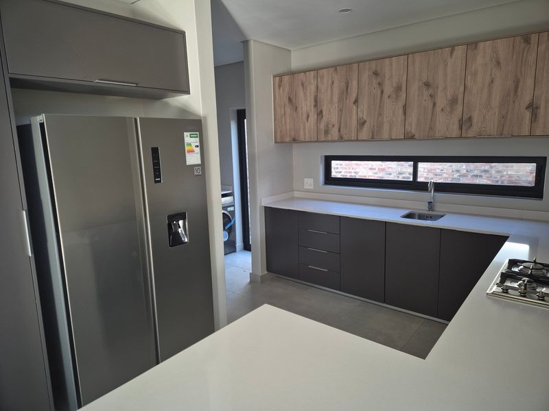 Modern kitchen featuring sleek dark cabinetry, wood-grain upper cabinets, stone countertops, and a gas hob, with an adjacent scullery area.