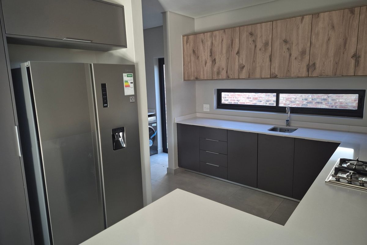 Modern kitchen featuring sleek dark cabinetry, wood-grain upper cabinets, stone countertops, and a gas hob, with an adjacent scullery area.