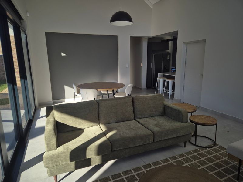 Spacious open-plan living and dining area featuring tiled floors, vaulted ceilings, and large sliding glass doors that provide ample natural light.