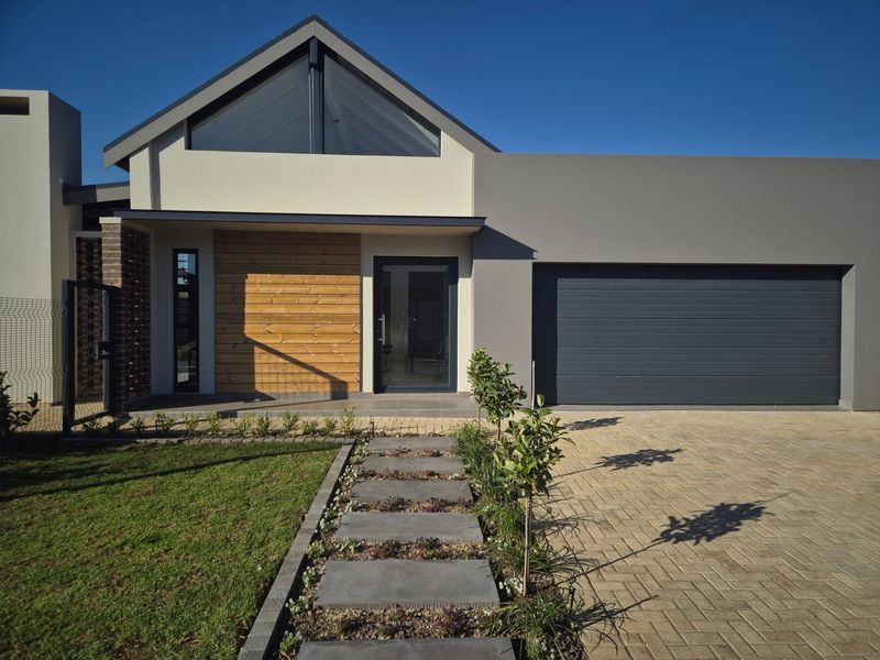 Modern townhouse front elevation featuring a paved driveway, sectional garage door, timber-clad accent wall, and a neat stone pathway leading to the entrance.