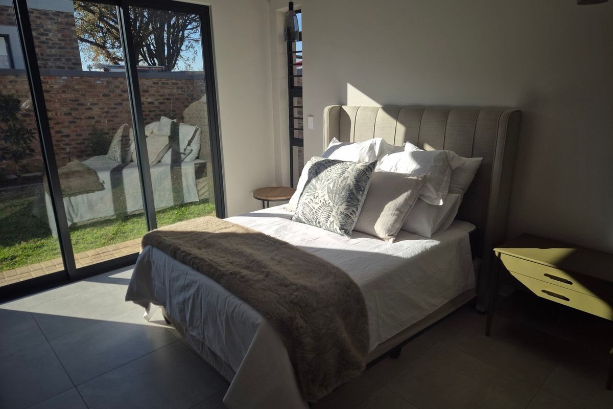 A bright, modern bedroom featuring large sliding glass doors that provide direct access to the garden and allow for ample natural light.