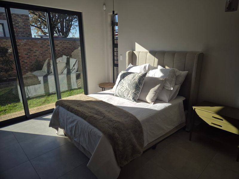 A bright, modern bedroom featuring large sliding glass doors that provide direct access to the garden and allow for ample natural light.