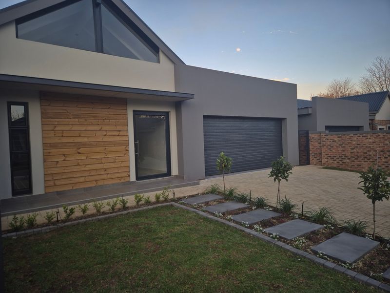 Modern townhouse exterior featuring a double garage, timber-clad facade, paved driveway, and a well-maintained front garden with a stone pathway.
