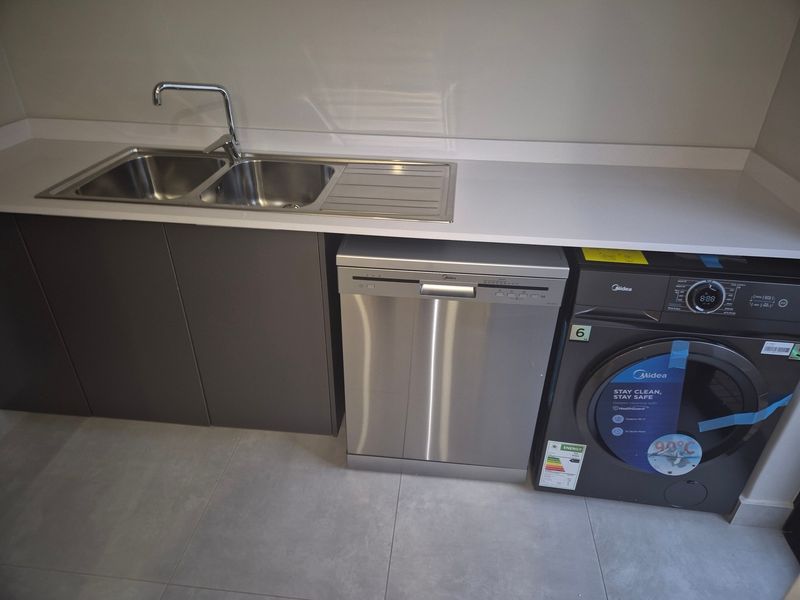 Modern scullery area featuring a double bowl stainless steel sink, stone countertops, built-in cabinetry, and integrated laundry and dishwashing appliances.