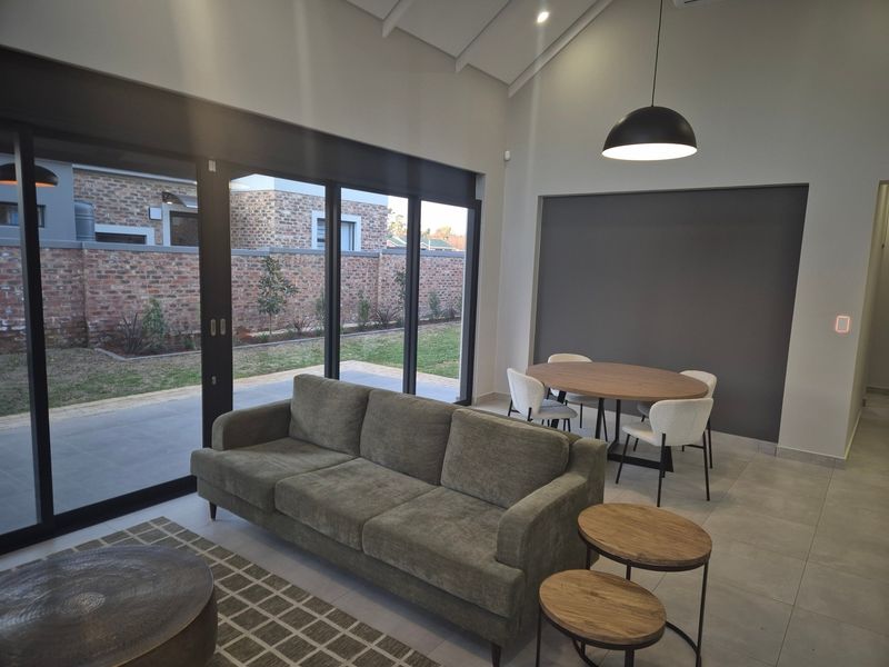Spacious open-plan living and dining area featuring vaulted ceilings, large sliding glass doors providing natural light, and modern tiled flooring.