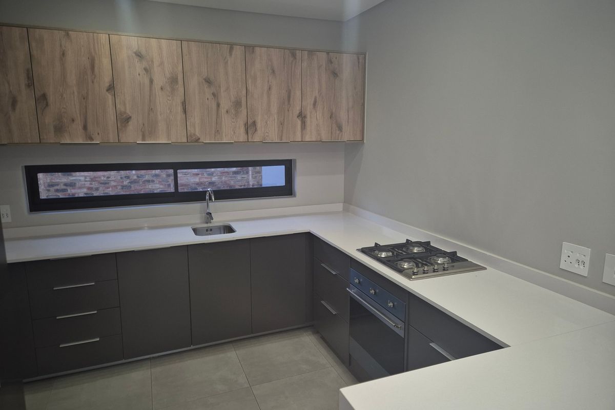 Modern kitchen featuring sleek dark grey lower cabinetry, wood-grain upper cabinets, white stone countertops, integrated gas hob, and built-in oven.