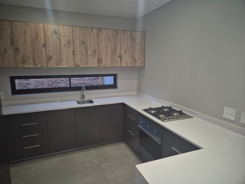 Modern kitchen featuring sleek dark grey lower cabinetry, wood-grain upper cabinets, white stone countertops, integrated gas hob, and built-in oven.
