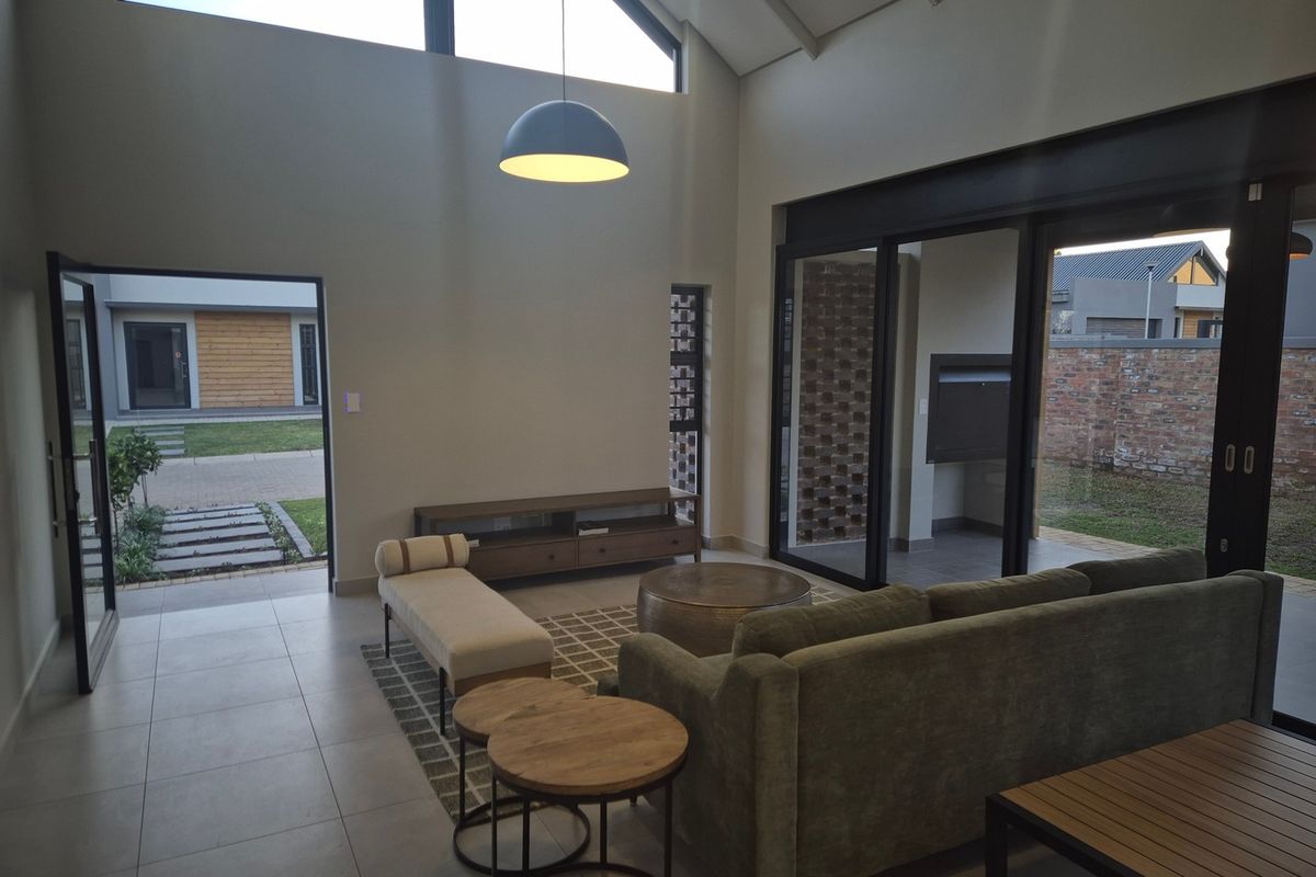 Spacious living room with high vaulted ceilings, exposed steel beams, and large sliding glass doors providing seamless access to the outdoor patio area.