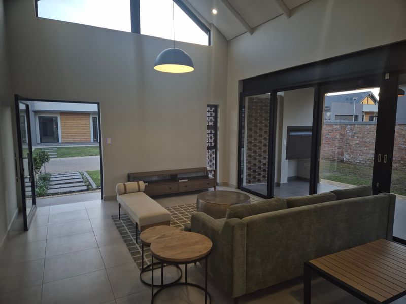 Spacious living room with high vaulted ceilings, exposed steel beams, and large sliding glass doors providing seamless access to the outdoor patio area.
