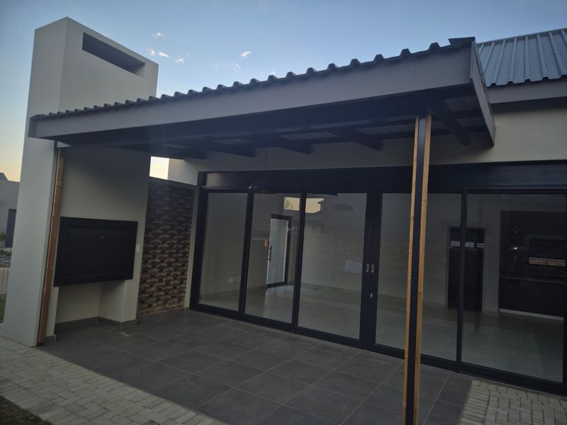 Covered patio area featuring a built-in braai, tiled flooring, and large sliding glass doors providing seamless access to the interior living space.