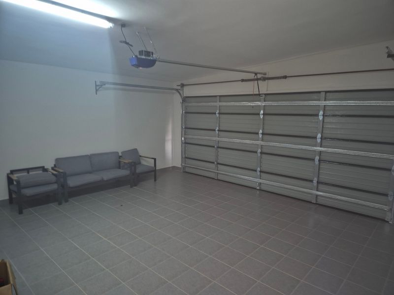 A clean and spacious double garage featuring tiled flooring, a sectional garage door, and an automated door motor.