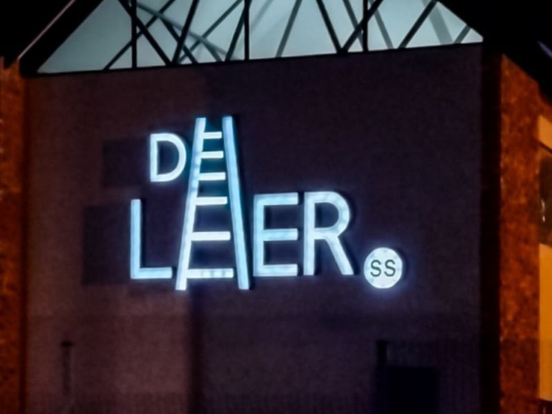 Night view of the apartment complex facade featuring illuminated building signage and a distinctive gabled architectural roof detail.
