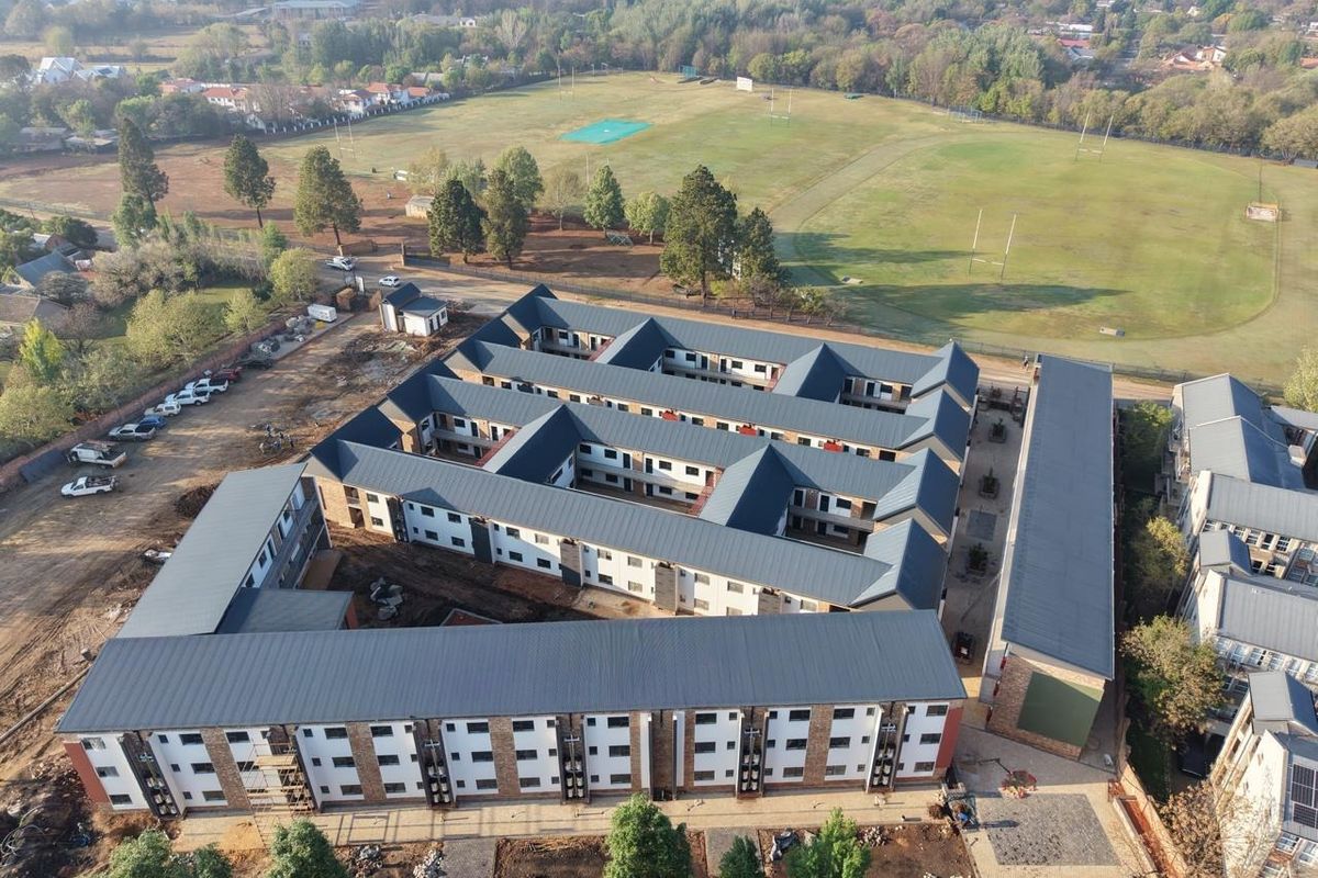 Aerial view of a multi-story apartment complex featuring pitched metal roofing, brick exterior finishes, and an internal courtyard layout under construction.