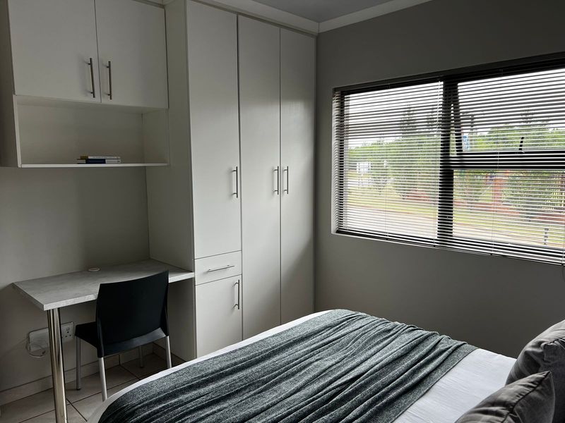 A well-maintained bedroom featuring built-in cupboards, a integrated desk workspace, and venetian blinds, offering a clean and functional living space.