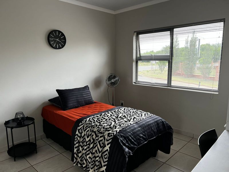 A well-maintained bedroom featuring neutral wall tones, tiled flooring, and a large window with fitted horizontal blinds.