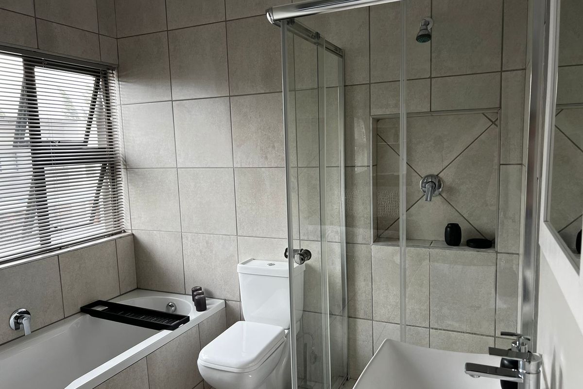 A modern, neutral-toned bathroom featuring a built-in bathtub, a glass-enclosed shower with a recessed niche, a toilet, and a vanity basin.