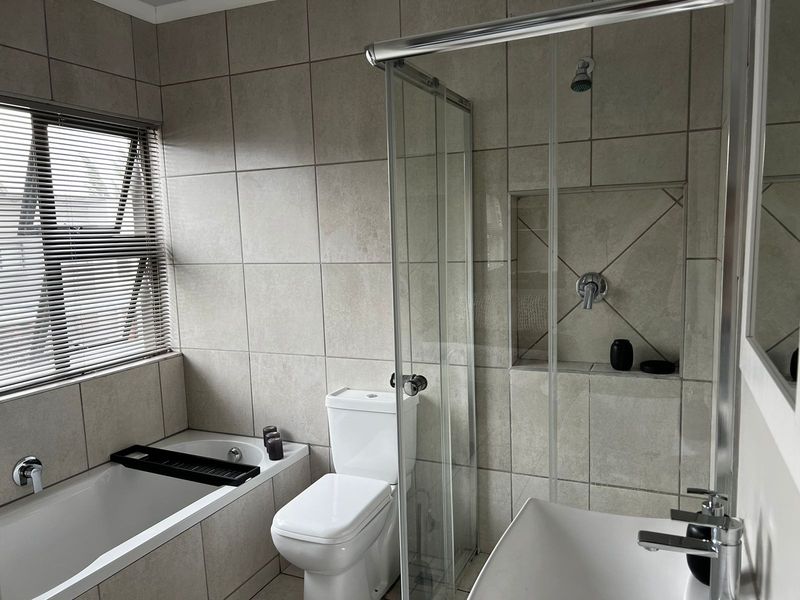 A modern, neutral-toned bathroom featuring a built-in bathtub, a glass-enclosed shower with a recessed niche, a toilet, and a vanity basin.