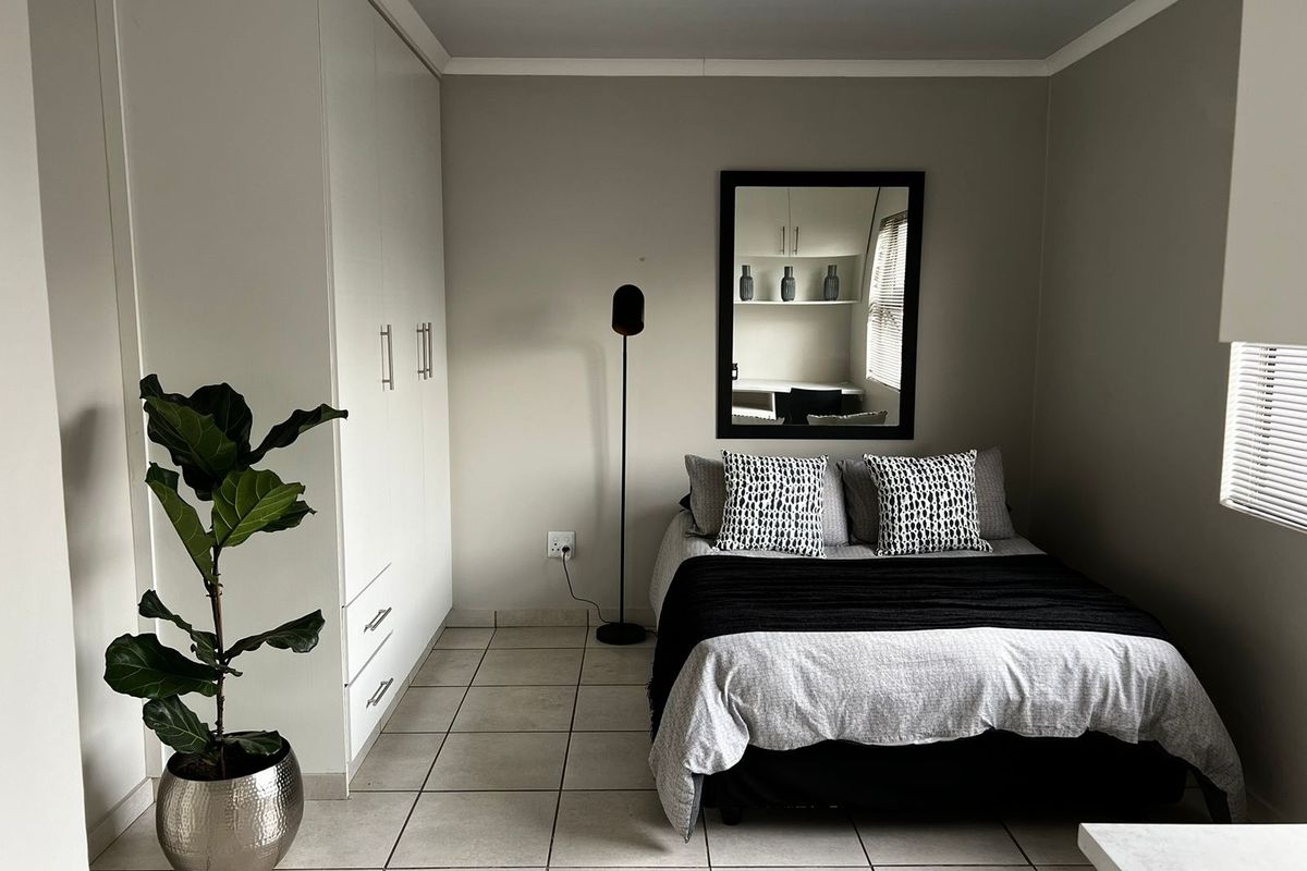 A well-maintained bedroom featuring neutral tiled flooring, built-in white cabinetry, and venetian blinds, offering a clean and functional living space.