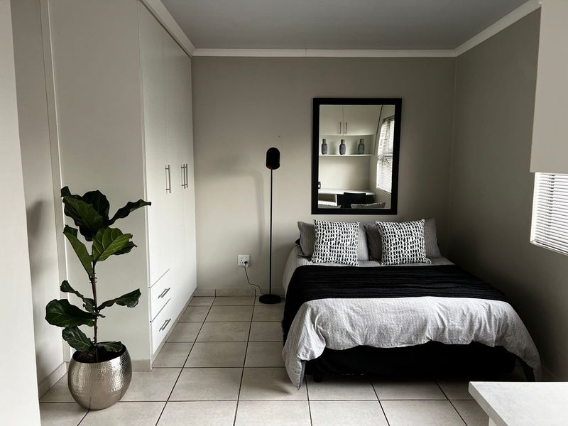 A well-maintained bedroom featuring neutral tiled flooring, built-in white cabinetry, and venetian blinds, offering a clean and functional living space.
