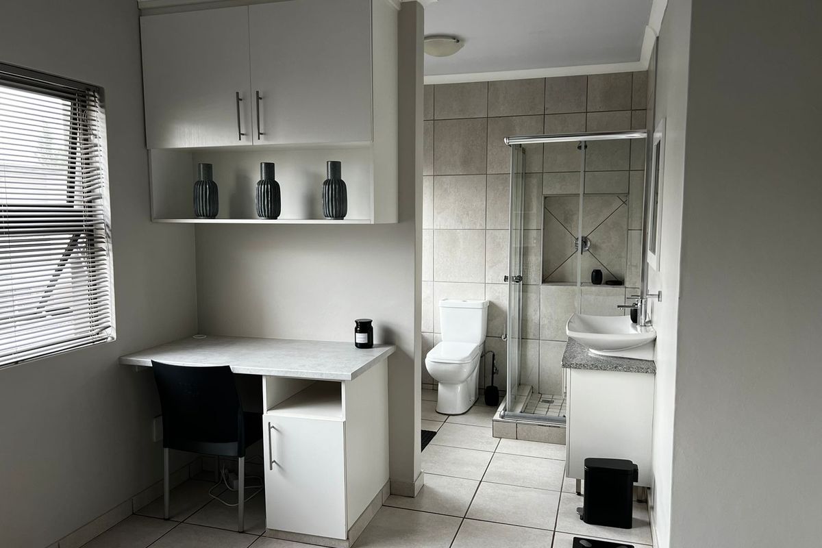 A modern bathroom featuring a built-in vanity with a vessel sink, a glass-enclosed shower, a toilet, and a convenient built-in desk area.