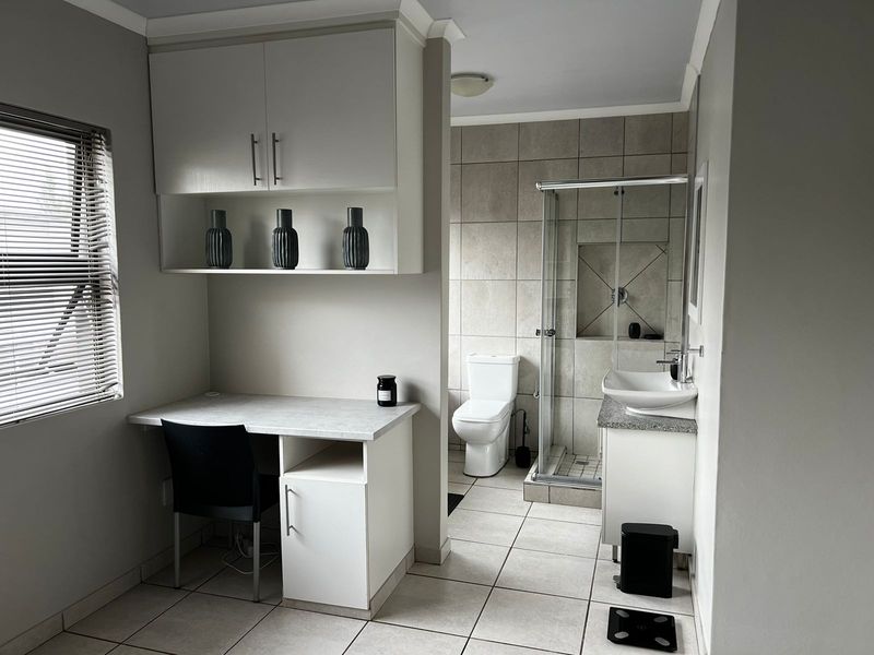 A modern bathroom featuring a built-in vanity with a vessel sink, a glass-enclosed shower, a toilet, and a convenient built-in desk area.