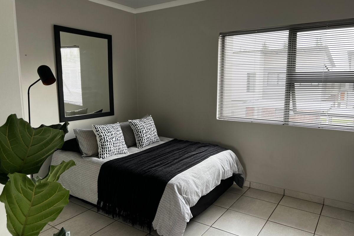 A well-maintained bedroom featuring neutral wall tones, tiled flooring, and venetian blinds, providing a clean and functional living space.