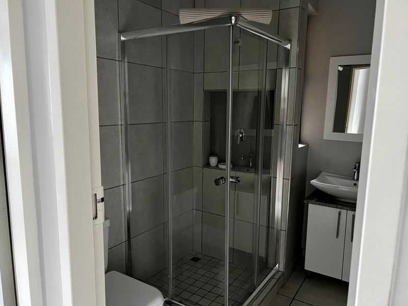 A modern bathroom featuring a glass shower enclosure with a built-in niche, a vanity cabinet with a vessel sink, and neutral wall and floor tiling.