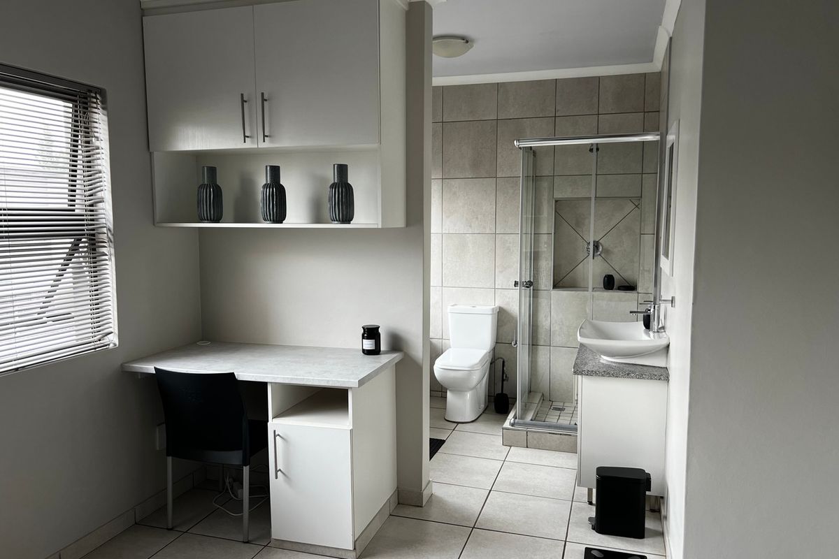 A modern bathroom featuring a glass shower enclosure, wall-mounted basin with vanity, and an integrated desk area with overhead storage cabinetry.