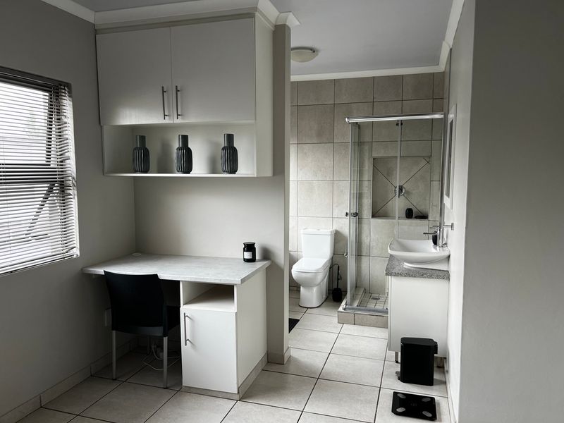 A modern bathroom featuring a glass shower enclosure, wall-mounted basin with vanity, and an integrated desk area with overhead storage cabinetry.