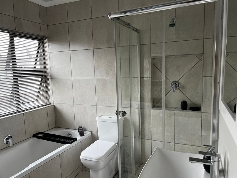 Modern bathroom featuring a tiled bathtub, a separate glass-enclosed shower with a recessed niche, a toilet, and a basin with contemporary fixtures.