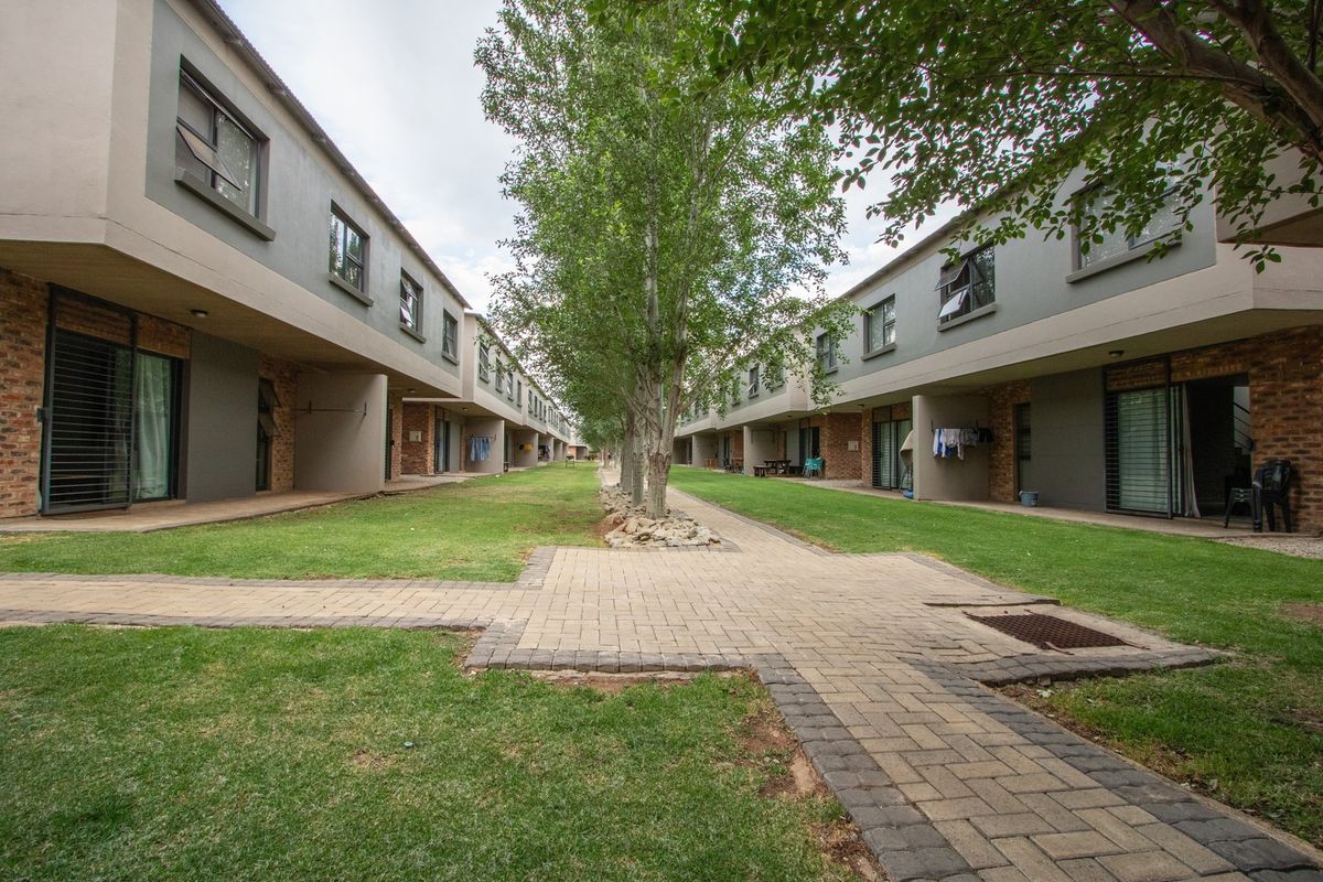 A view of the communal garden area between apartment blocks, featuring paved walkways, manicured lawns, and mature trees.