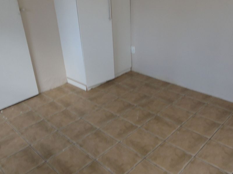 An empty bedroom featuring tiled flooring and a built-in cupboard, requiring minor cosmetic updates to the flooring and skirting.