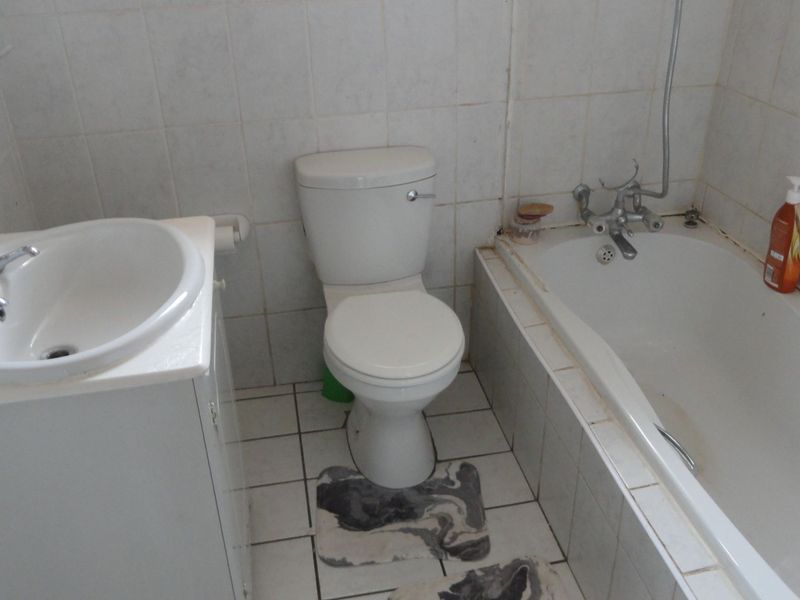 A functional bathroom featuring a vanity basin, toilet, and bathtub with tiled finishes, requiring cosmetic updates to improve its overall condition.