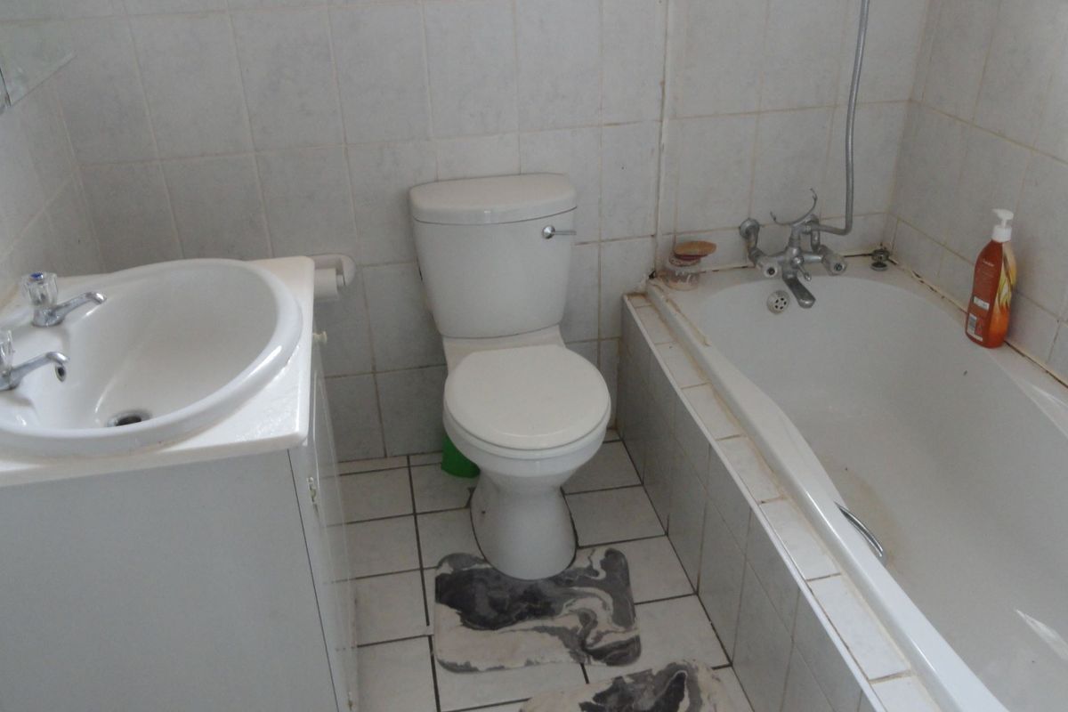 A functional bathroom featuring a vanity basin, toilet, and bathtub with tiled finishes, requiring cosmetic updates to improve its overall condition.