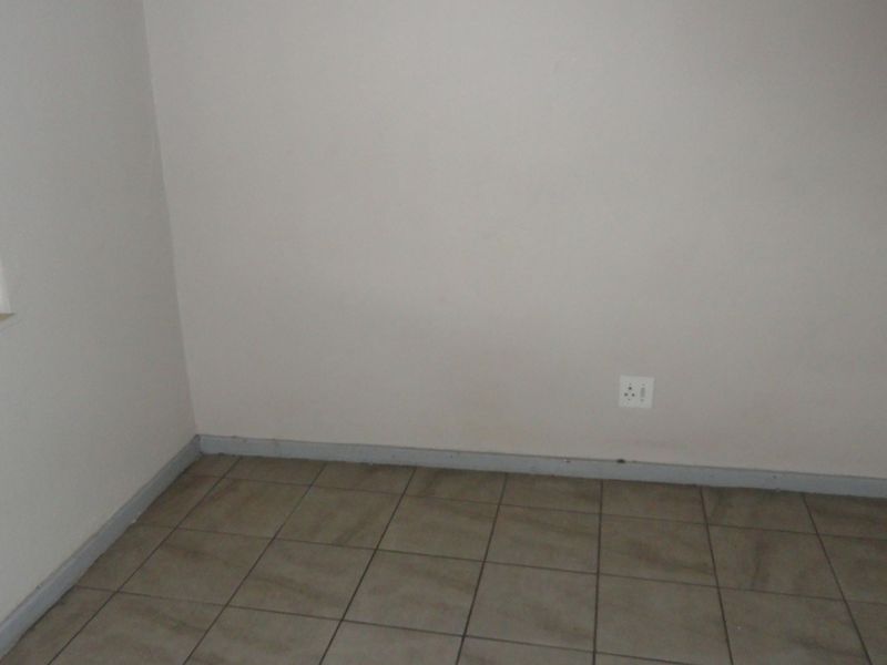 An empty bedroom featuring tiled flooring, neutral walls, and a window with security bars, providing a blank canvas for interior design.