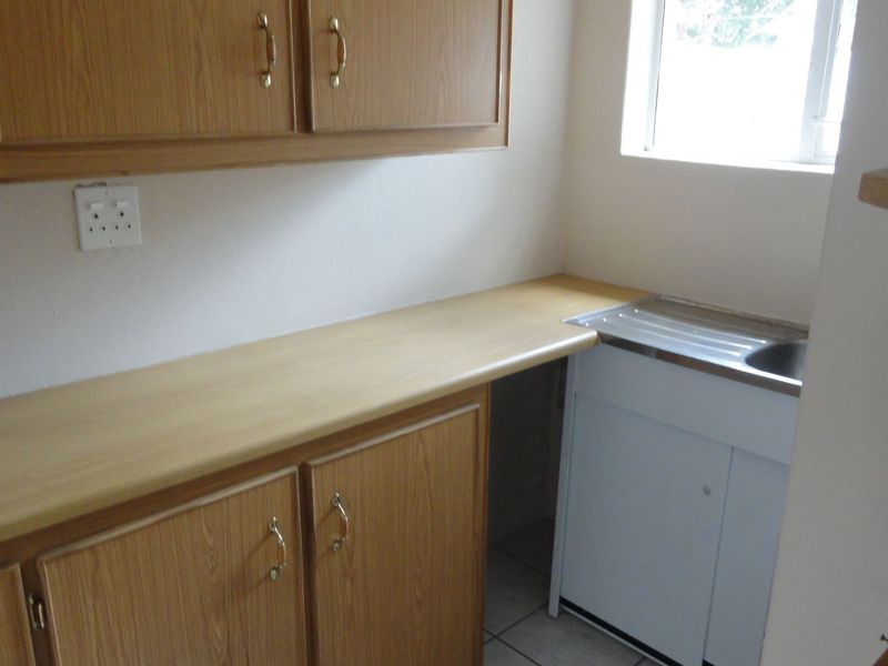 A functional scullery area featuring laminate cabinetry, a laminate countertop, and a stainless steel sink with tiled flooring.