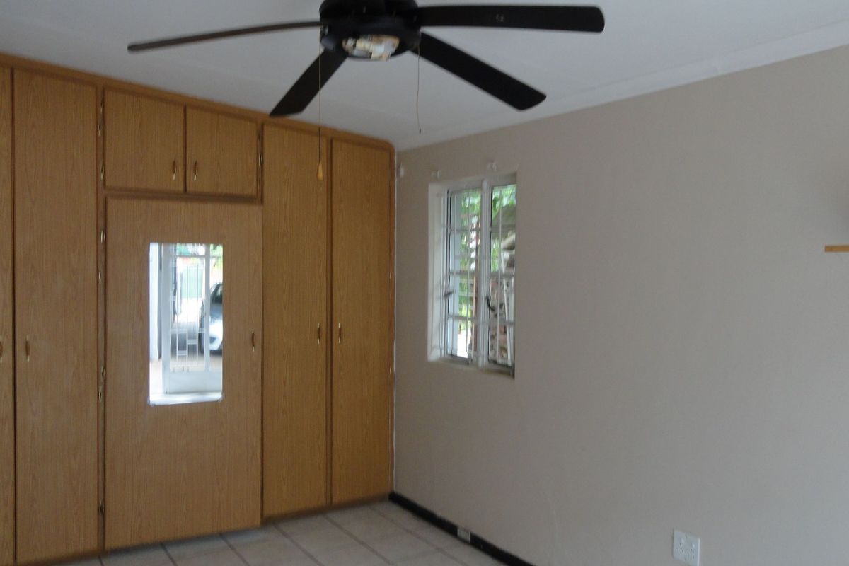 A spacious bedroom featuring built-in wooden cupboards, tiled flooring, and a ceiling fan, offering a neutral canvas for personalization.