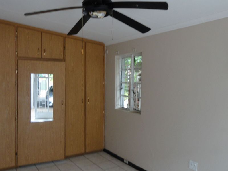 A spacious bedroom featuring built-in wooden cupboards, tiled flooring, and a ceiling fan, offering a neutral canvas for personalization.