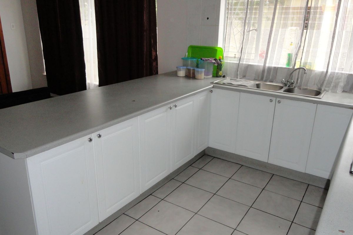 A functional kitchen featuring white cabinetry, grey laminate countertops, a double basin sink, and tiled flooring with an integrated hob.