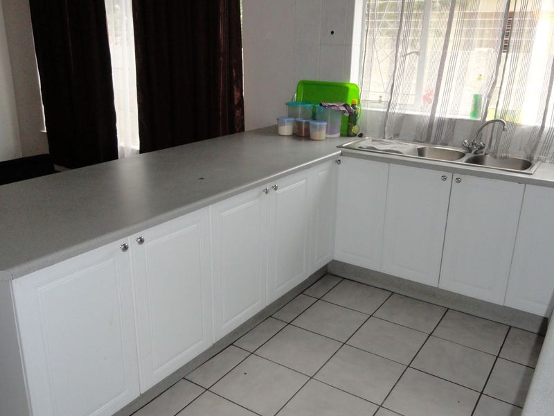 A functional kitchen featuring white cabinetry, grey laminate countertops, a double basin sink, and tiled flooring with an integrated hob.