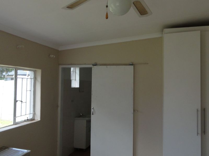 A vacant bedroom featuring built-in cupboards, a ceiling fan, and a sliding door leading to an en-suite bathroom.