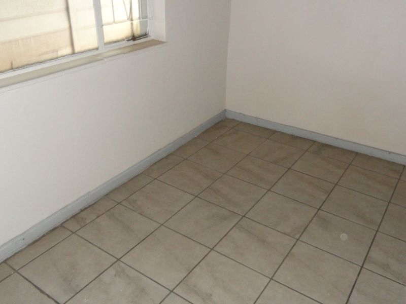 An empty bedroom featuring neutral wall paint, tiled flooring, and a window, providing a blank canvas for potential interior design updates.