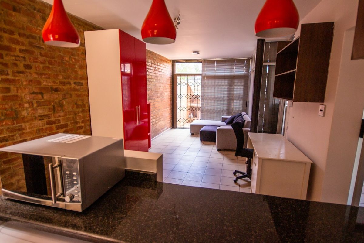 Open-plan living area featuring exposed brick walls, tiled flooring, and a kitchen with granite countertops, leading to a secure patio entrance.
