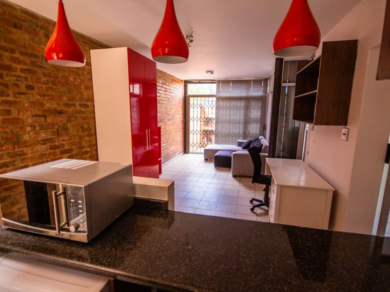 Open-plan living area featuring exposed brick walls, tiled flooring, and a kitchen with granite countertops, leading to a secure patio entrance.