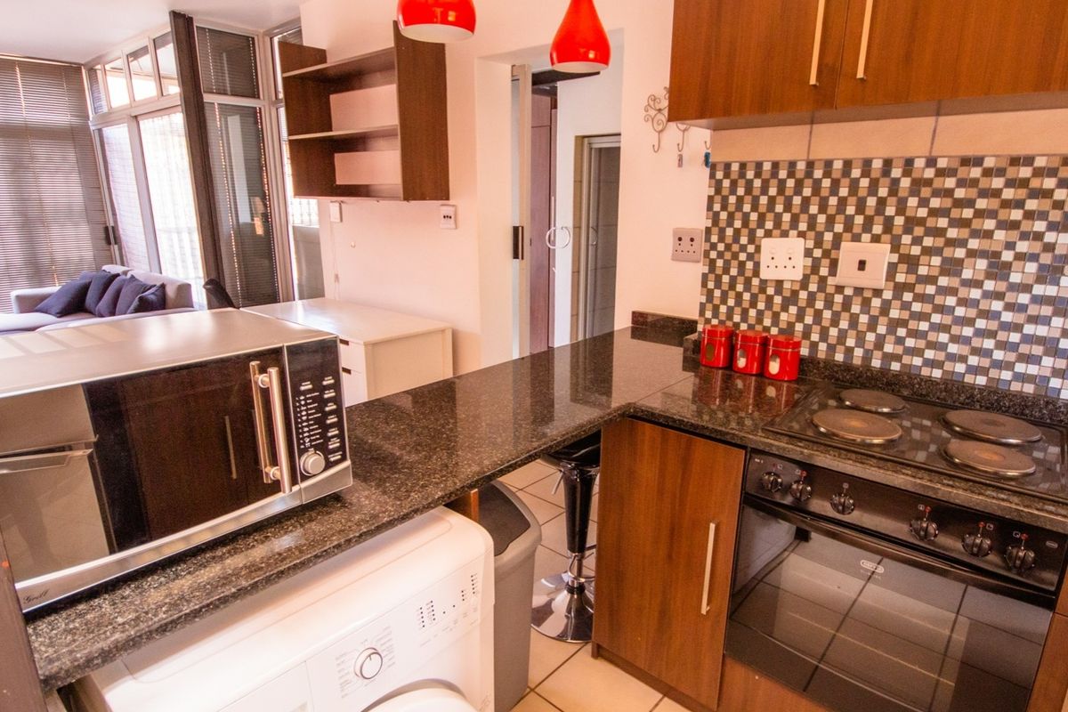 Open-plan kitchen featuring granite countertops, built-in oven, electric hob, and mosaic tile backsplash, seamlessly flowing into the adjacent living area.