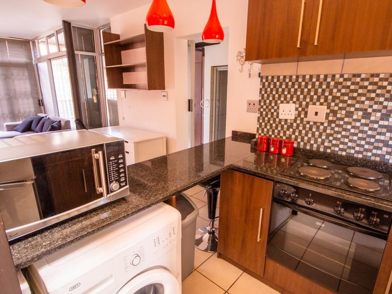 Open-plan kitchen featuring granite countertops, built-in oven, electric hob, and mosaic tile backsplash, seamlessly flowing into the adjacent living area.
