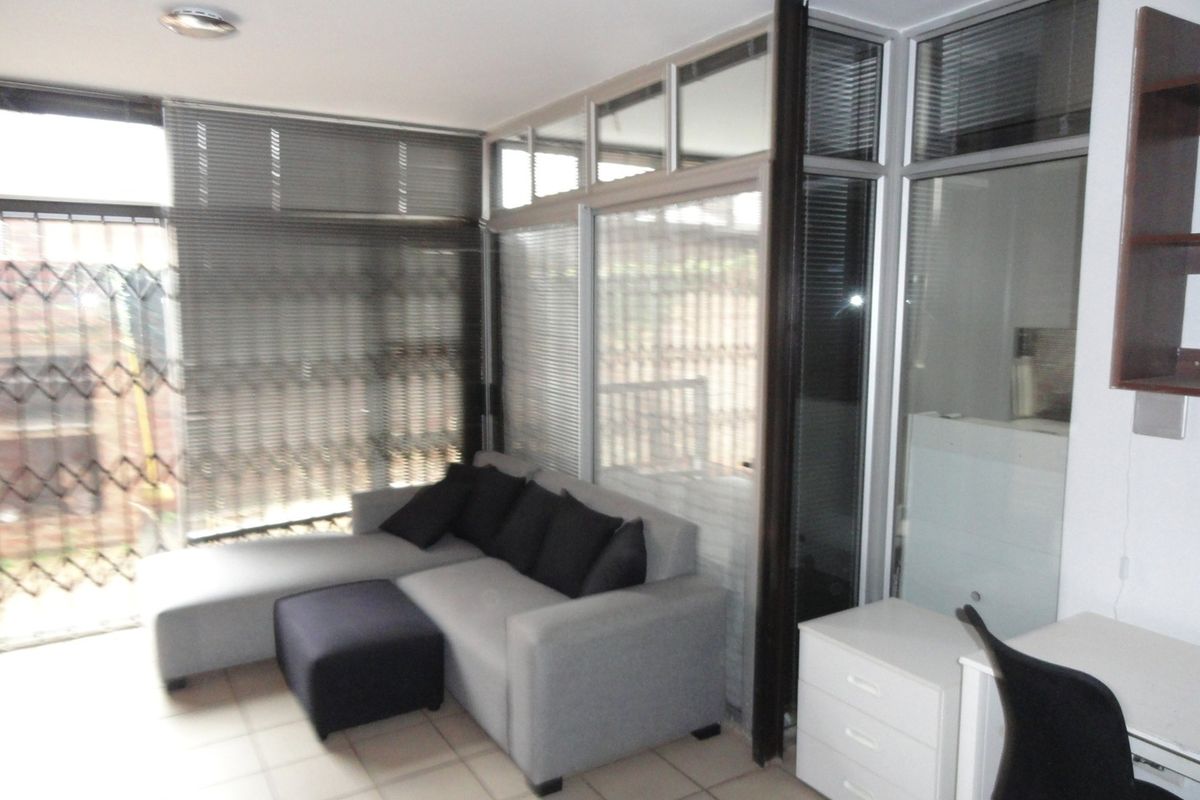 Living area featuring tiled flooring, large aluminium-framed windows with venetian blinds, and a glass partition wall providing separation.