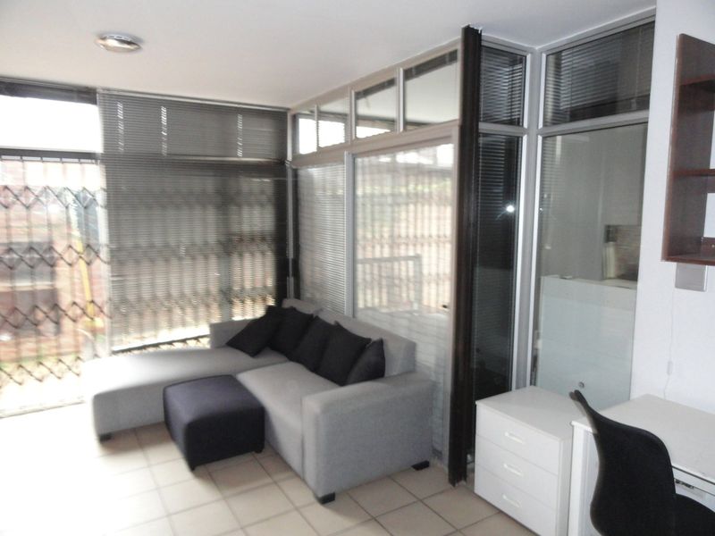 Living area featuring tiled flooring, large aluminium-framed windows with venetian blinds, and a glass partition wall providing separation.