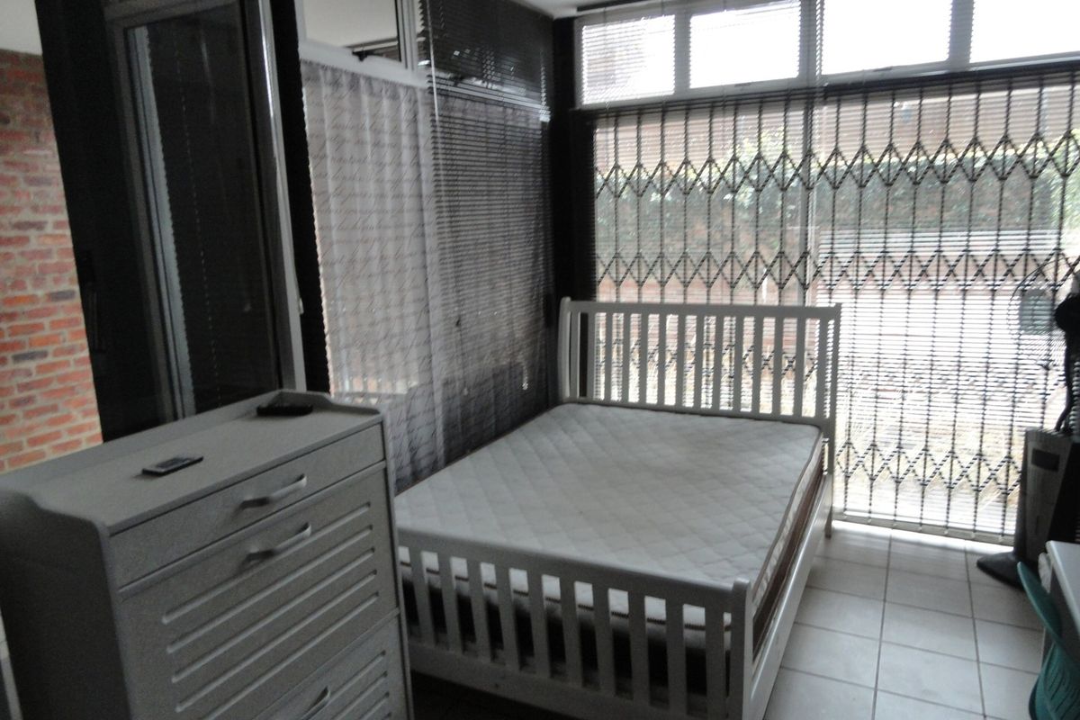 A bedroom featuring tiled flooring, large windows with security gates, and natural light, offering a functional space ready for personal touches.